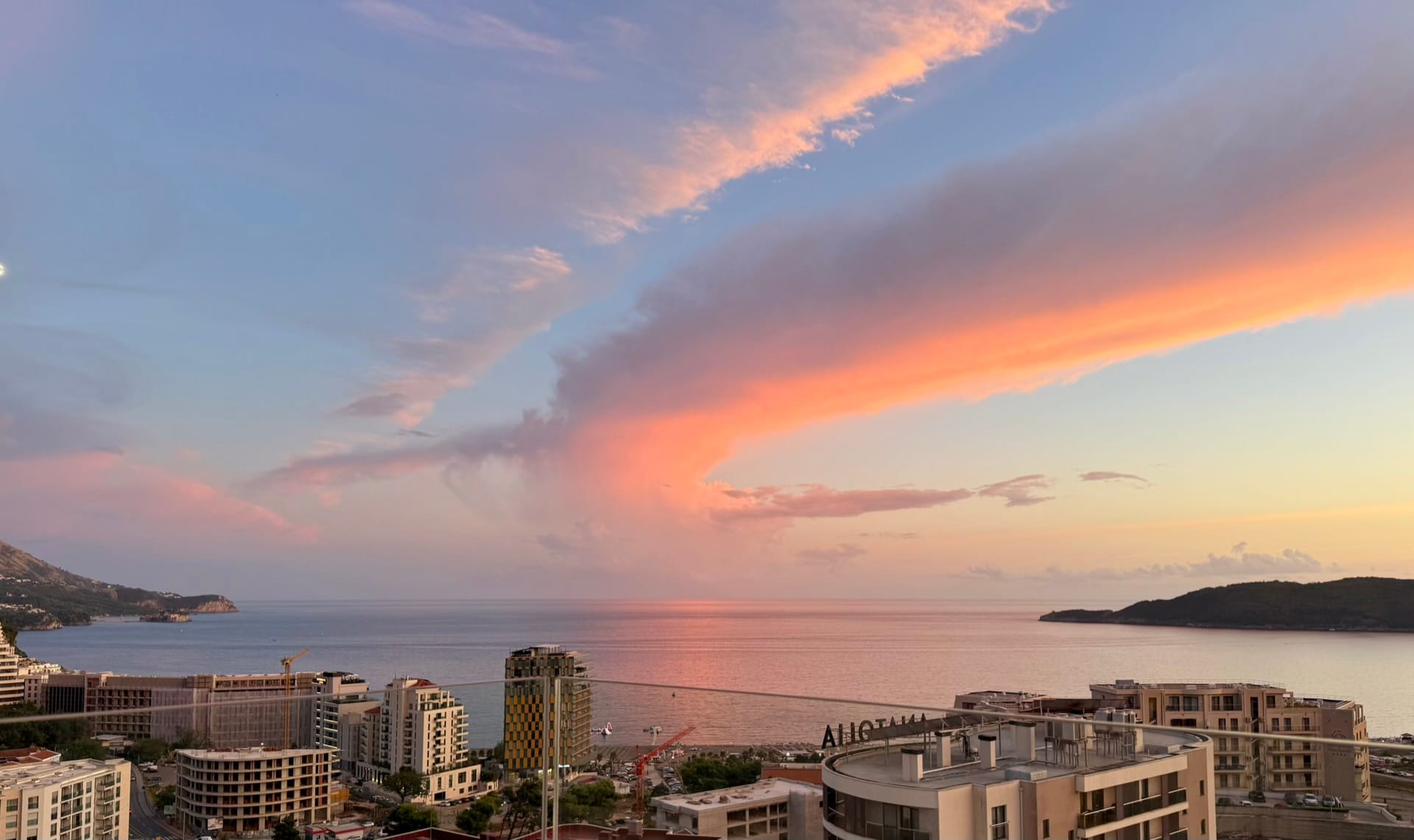 Panoramic sea and sunset view from the apartment balcony in Bečići, Montenegro, overlooking the coastline and modern buildings.
