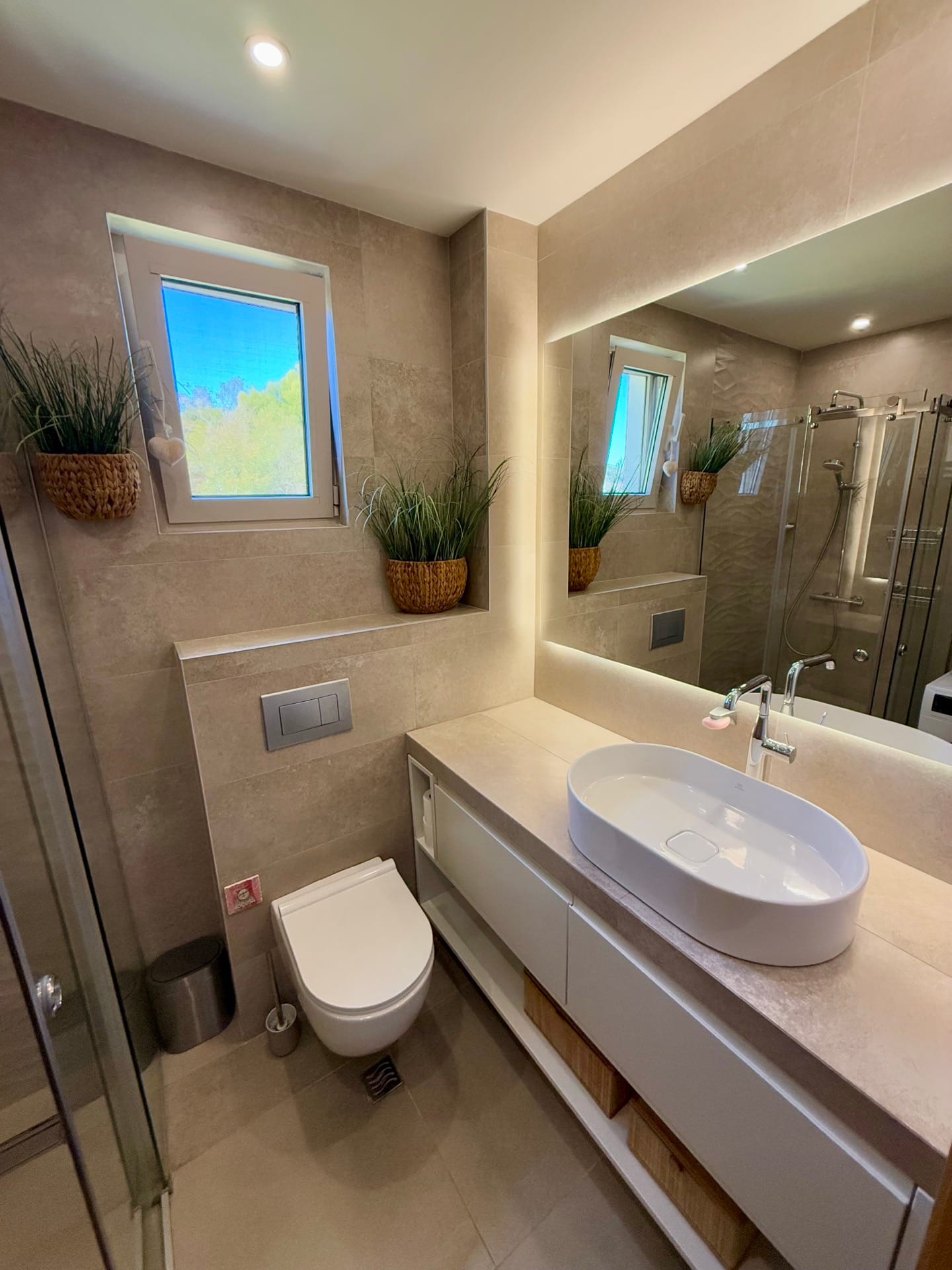 Modern bathroom in an apartment in Bečići, Montenegro: shower cabin, countertop sink, and illuminated mirror.