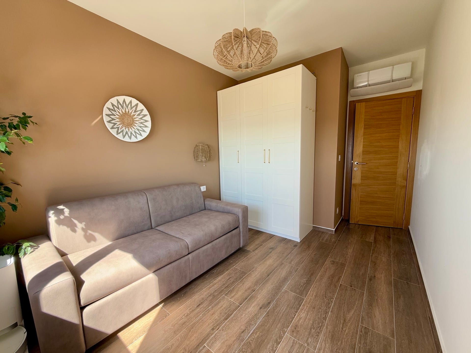 Living room in an apartment in Bečići, Montenegro: beige sofa, white cabinet, wooden floor, and woven light fixture.