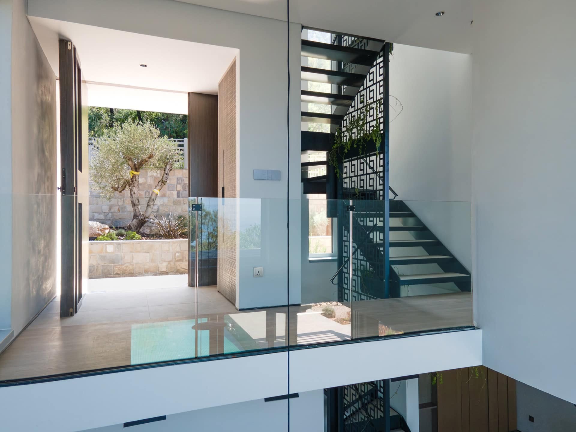 Modern villa interior in Blizikuće, Montenegro: designer staircase, glass railings, and access to the garden.
