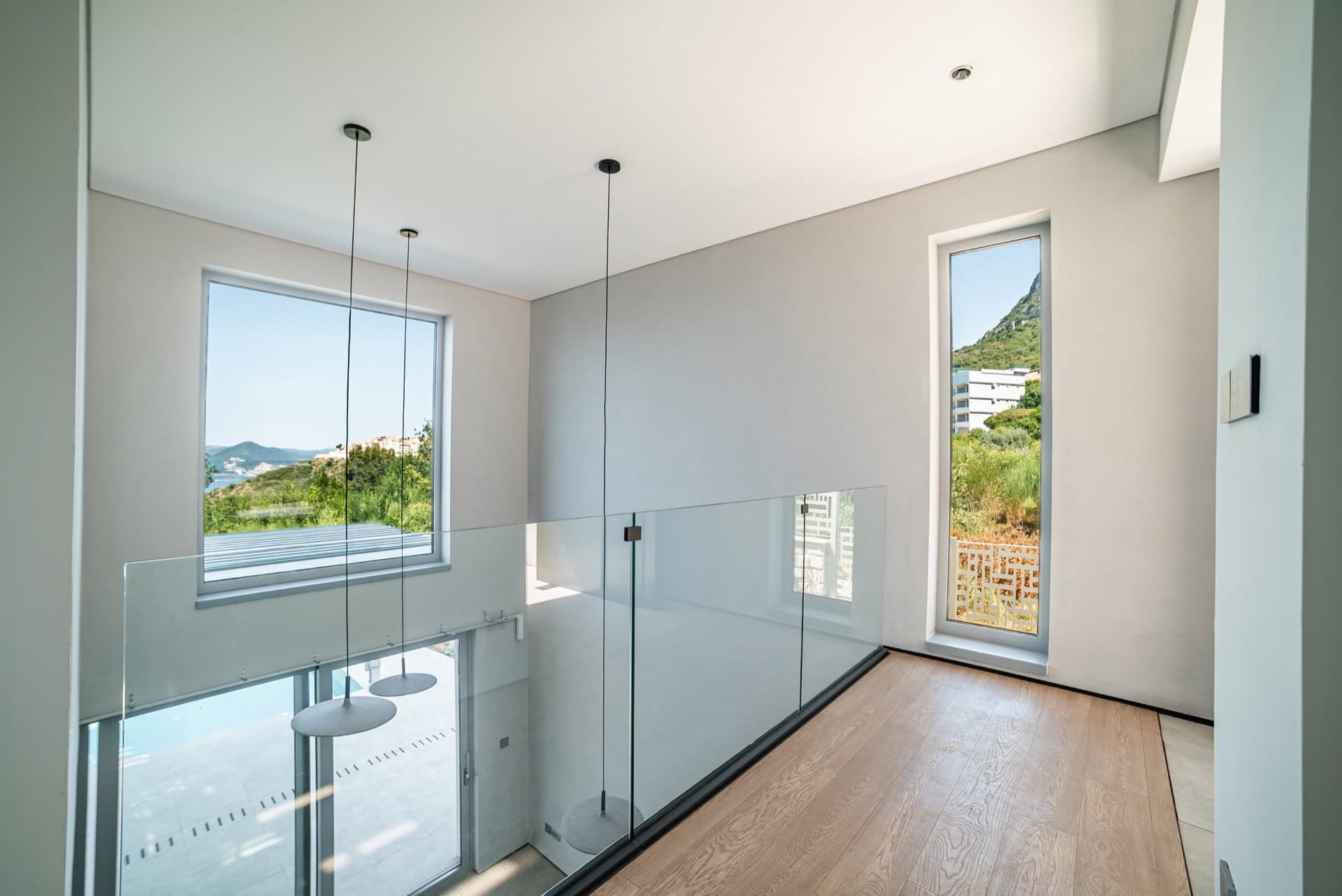 Modern villa living room in Blizikuće, Montenegro: glass railings, panoramic windows, and views of the mountains and sea.