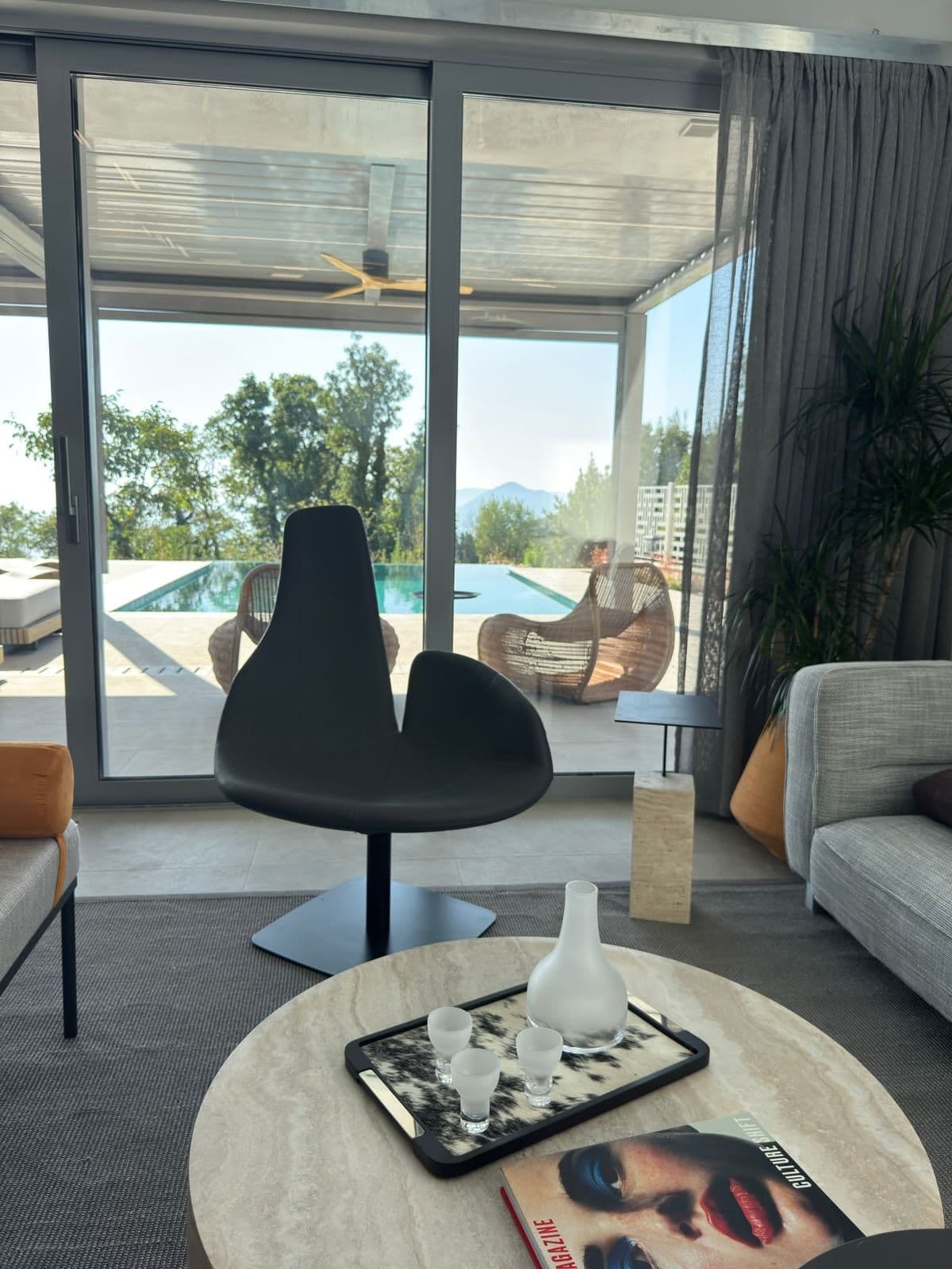 Villa living room in Blizikuće, Montenegro: panoramic windows, pool view, designer chair, and marble side table.