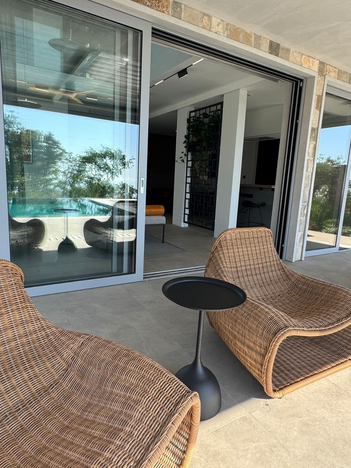 Villa terrace in Blizikuće, Montenegro: wicker chairs, panoramic windows, and a view of the pool in a modern interior.