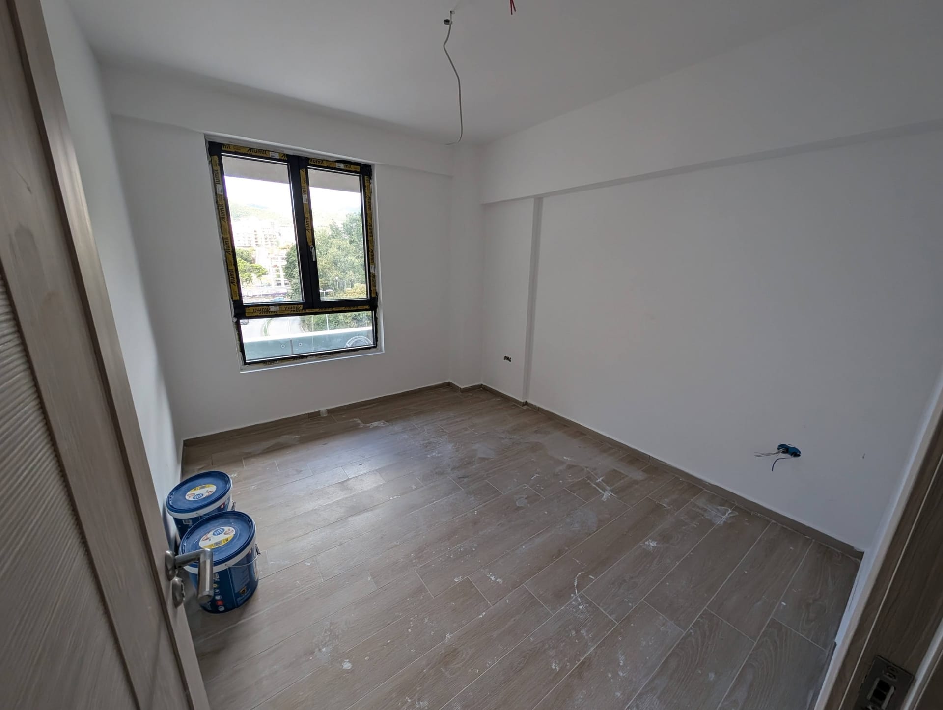 Bedroom in a new building in Rafailovici, Montenegro: white walls, wood-look floor tiles, mountain view from the window.