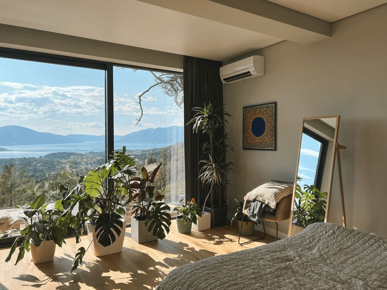 Bedroom with panoramic sea and mountain views in Kavač residential complex, Montenegro: stylish interior, lots of plants, and a floor mirror