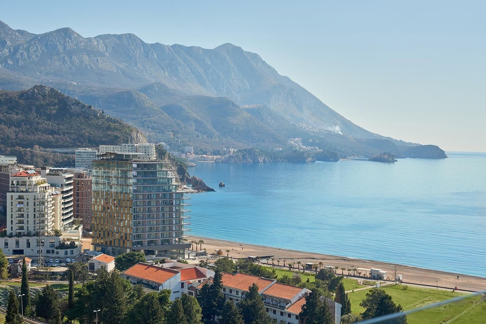 Panoramic view of the sea, beach, and mountains in Bečići, Montenegro, with modern residential complexes along the coast.