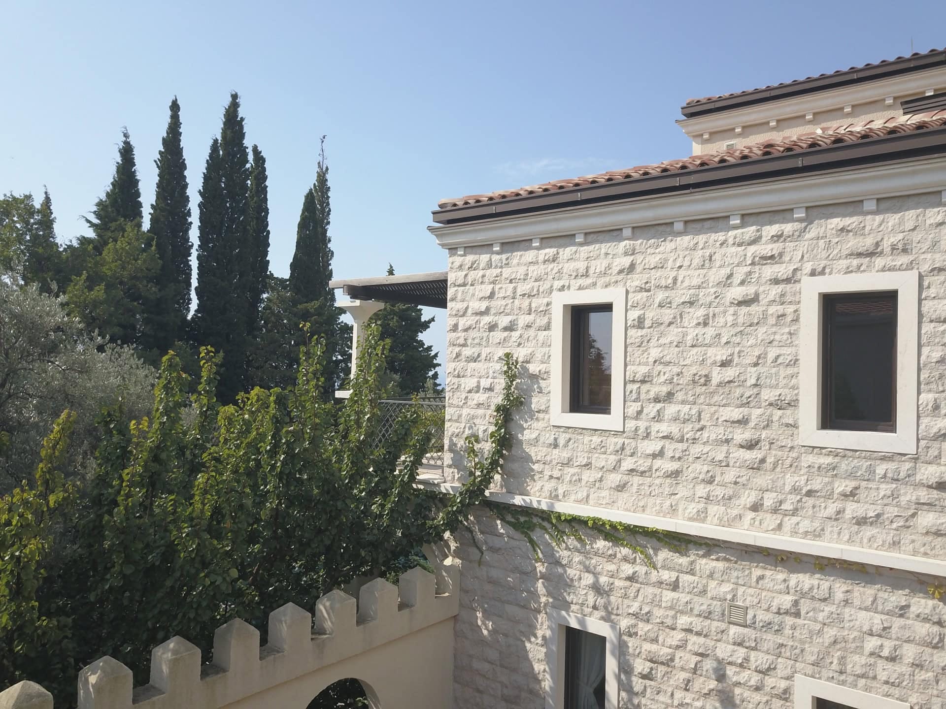 Villa facade of natural stone with a terrace and garden in Reževići, Montenegro: exterior view of the house with cypress trees.