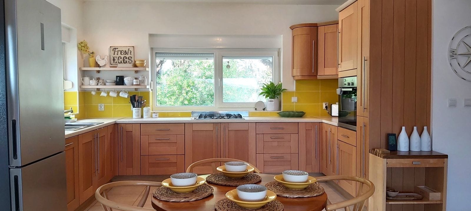 Cozy kitchen with wooden cabinets and a yellow backsplash in a house, Krymovitsa, Montenegro. Dining area and garden view.