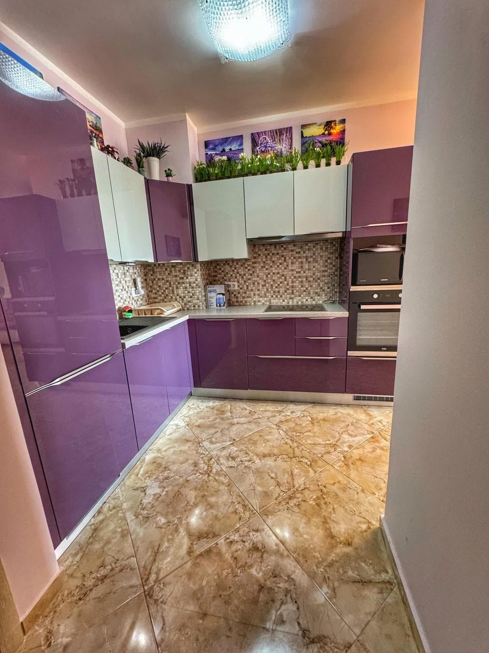 Modern kitchen with purple cabinets in an apartment, Dobri Vody, Montenegro: marble-look tile and built-in appliances.