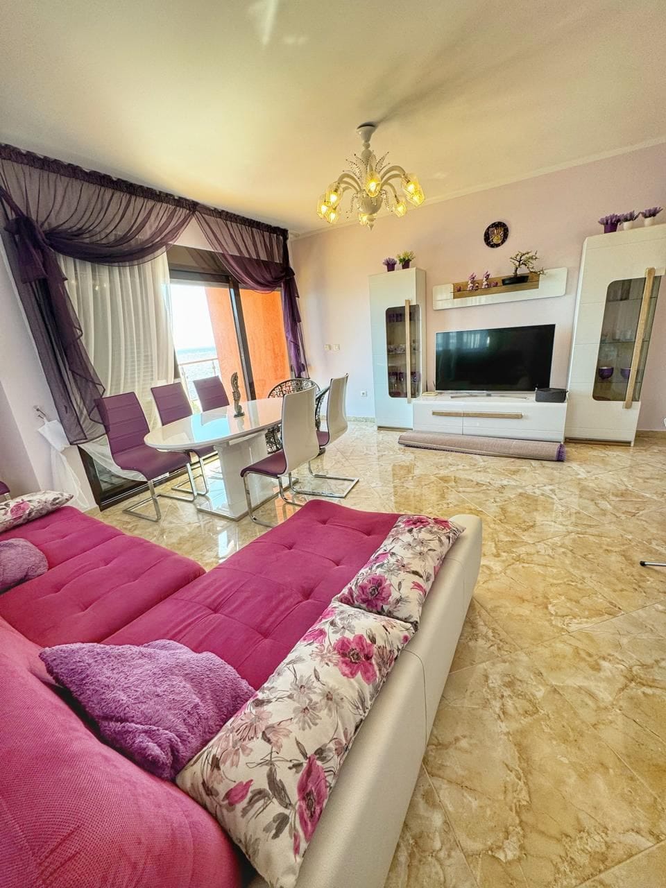 Living room in an apartment in Dobri Vody, Montenegro: pink sofa, dining area, panoramic windows, and light finishes.
