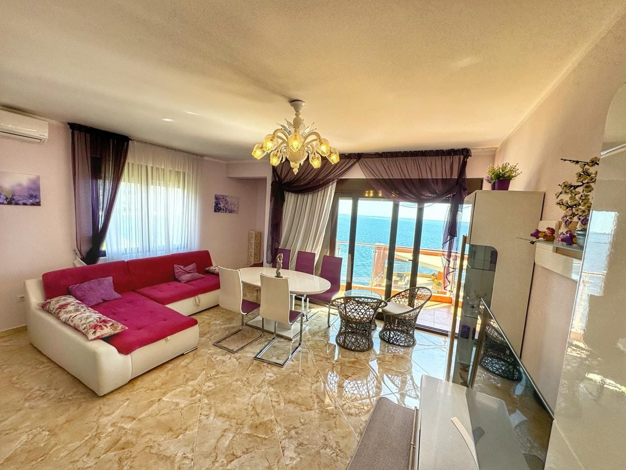Living room with sea view in an apartment, Dobri Vody, Montenegro: red sofa, dining area, and panoramic windows.