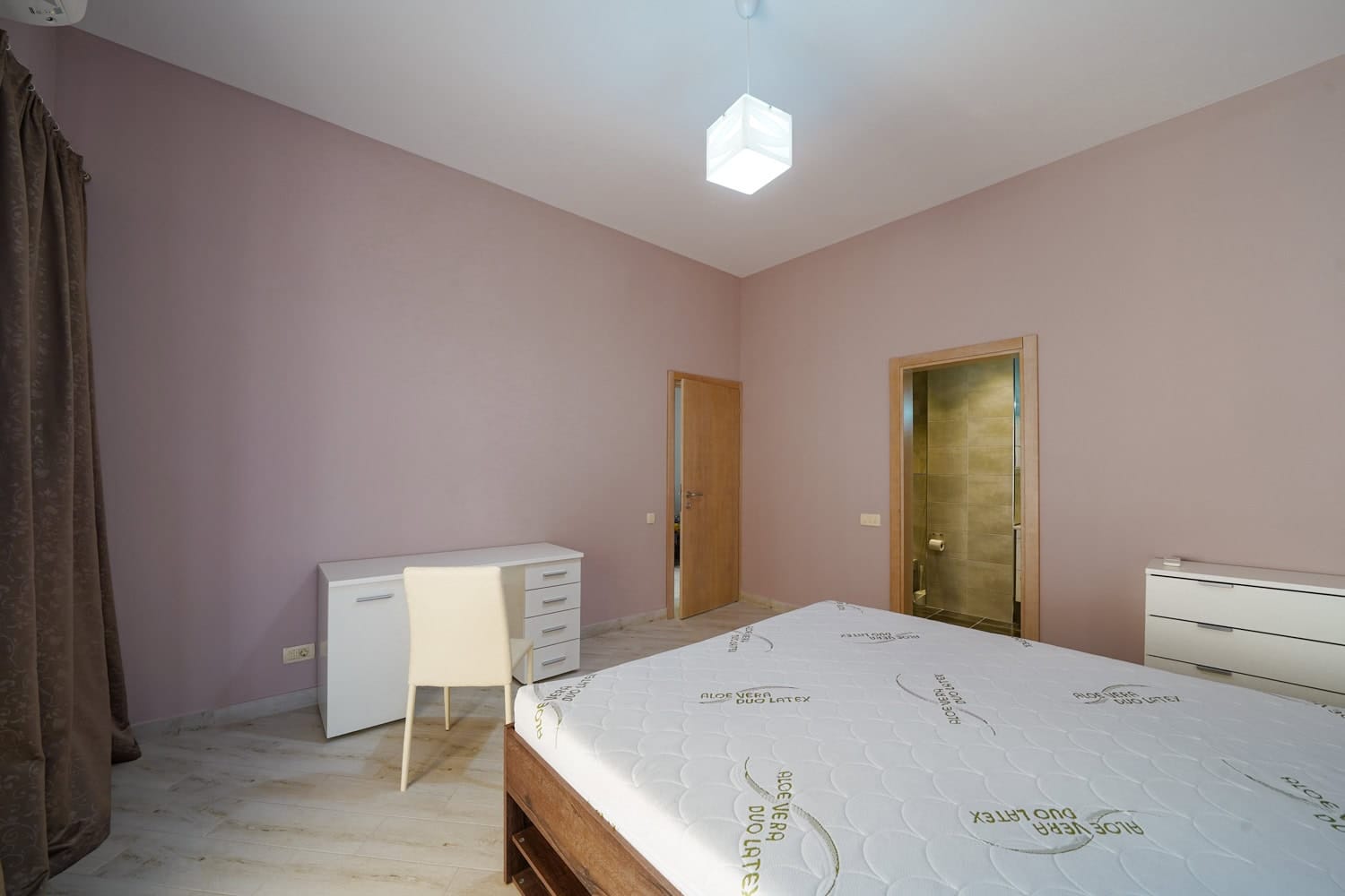 Bedroom in an apartment in Bečići, Montenegro: double bed, white desk, dresser, and entrance to the bathroom.