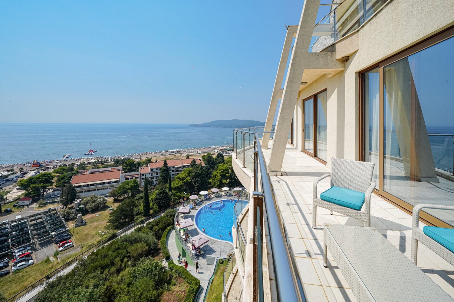 Spacious balcony with furniture and panoramic views of the sea, beach, and swimming pool in Bečići, Montenegro.