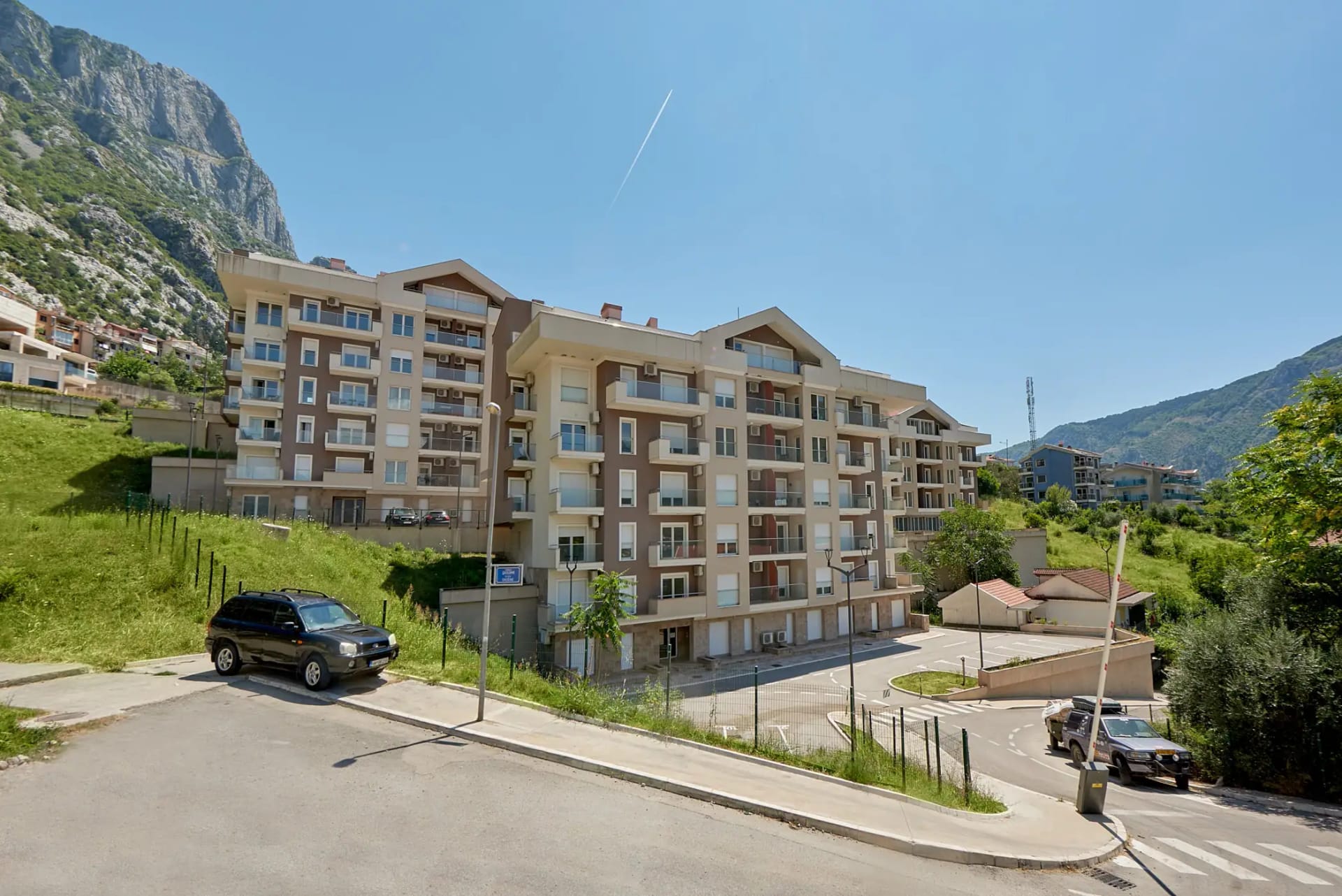 Modern residential complex in Dobrota, Montenegro: view of an apartment building with parking and mountain landscape.