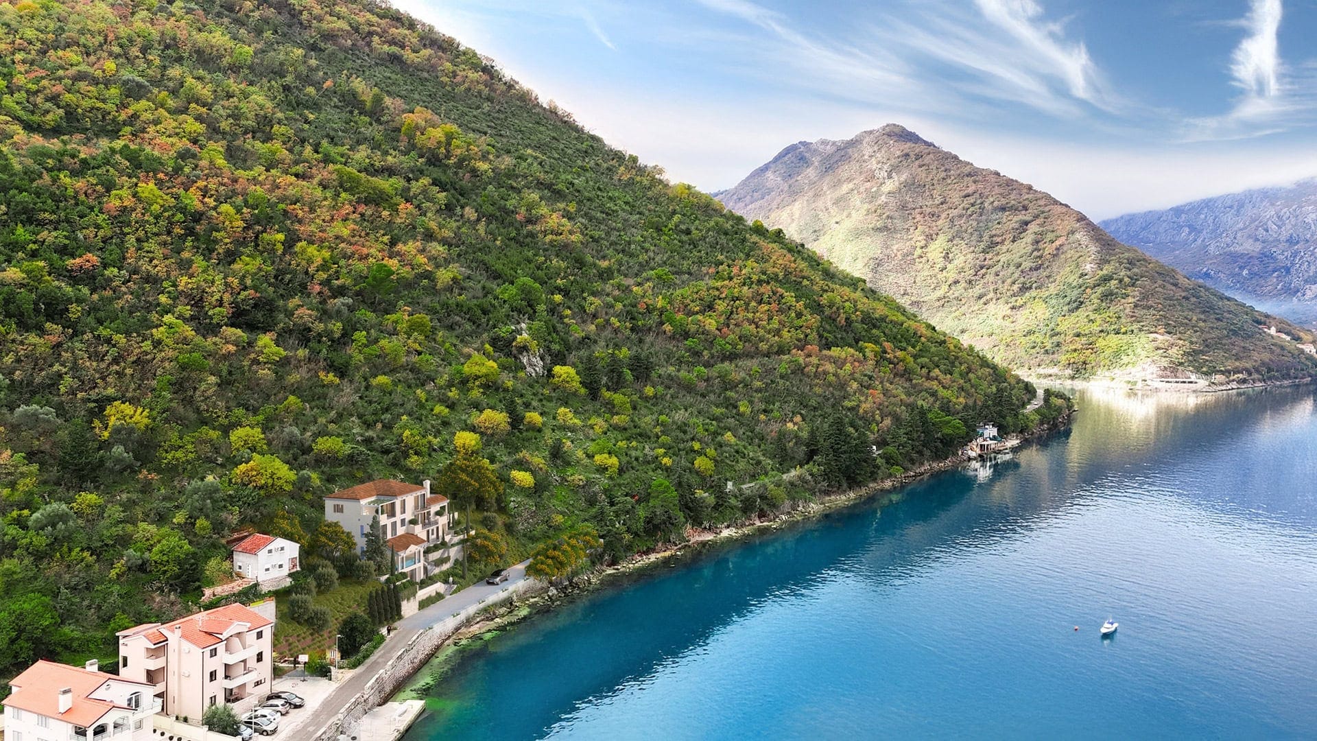Aerial view of a villa in Stoliv, Montenegro: a house by the sea with green mountains and the Bay of Kotor in the background.