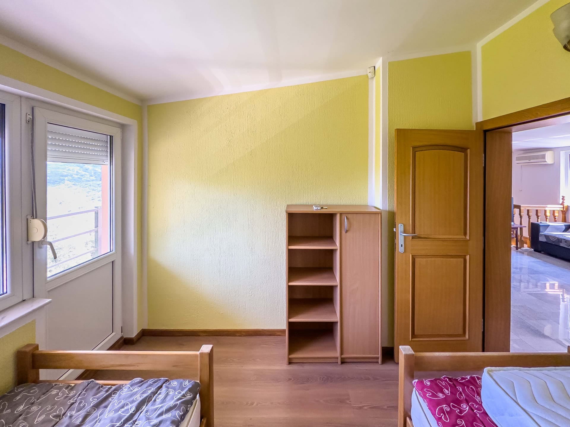 Bedroom in a house in Utjeha, Montenegro: yellow walls, wooden beds, a wardrobe, and access to a balcony with mountain views.