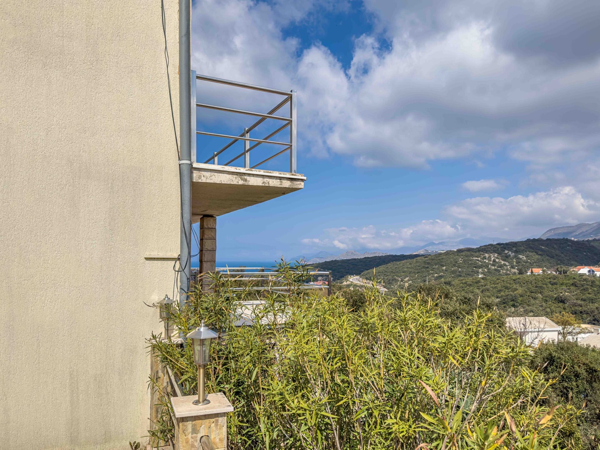 Balcony with a metal railing in a house in Utjeha, Montenegro, with panoramic views of the sea, mountains, and greenery.