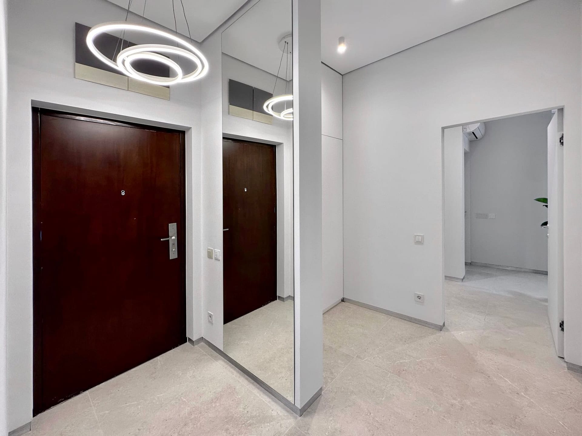 Modern hallway in an apartment, Bečići, Montenegro: light-toned finishes, large mirror, and designer chandelier.