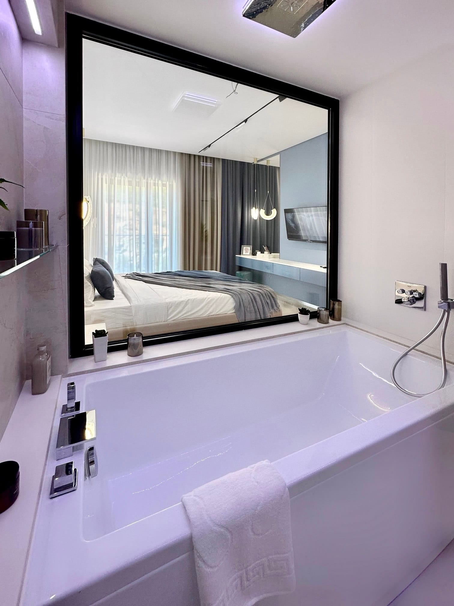 Modern bathroom with a panoramic window looking into the bedroom in an apartment in Becici, Montenegro. White bathtub, stylish interior.