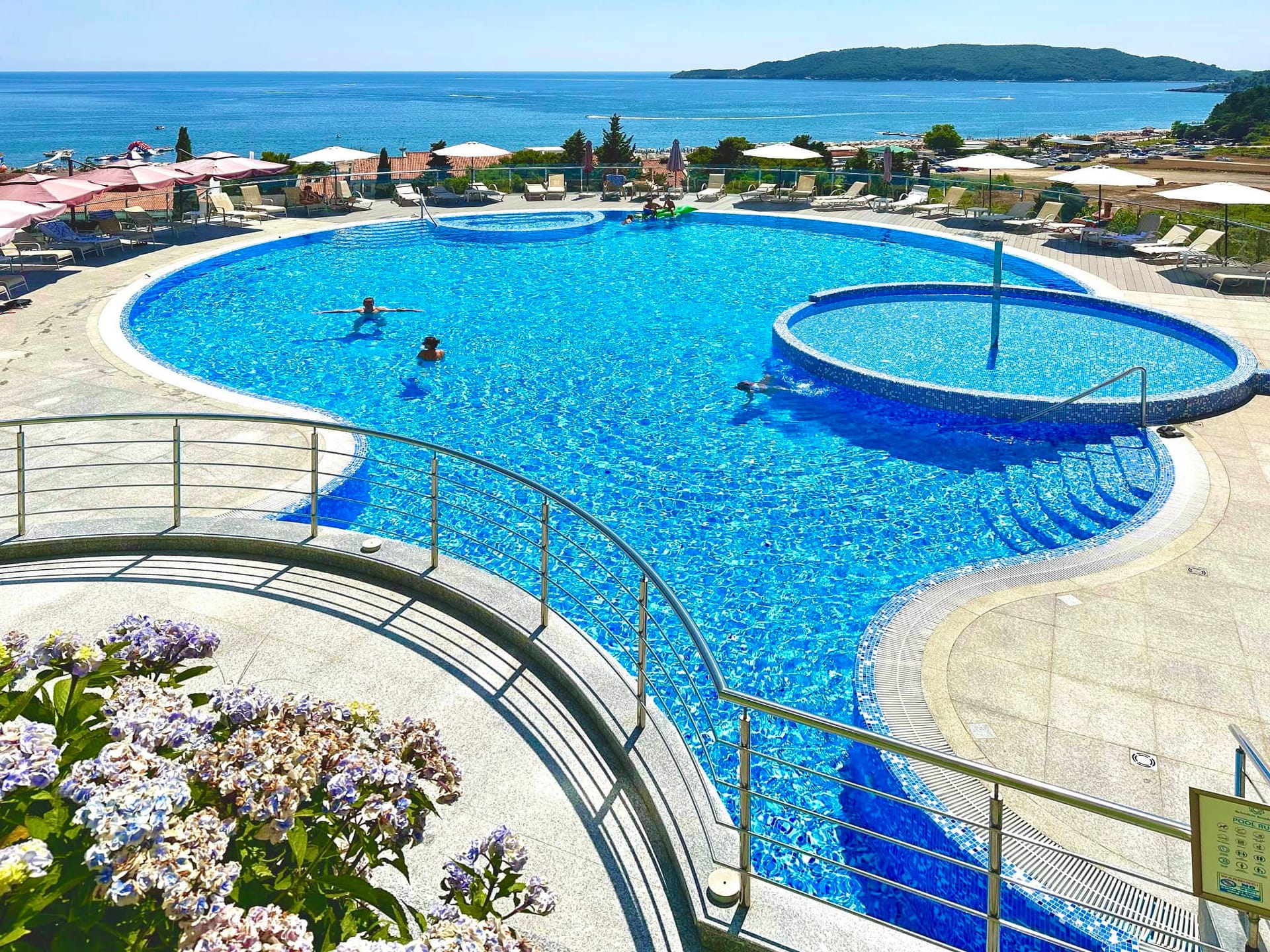 Outdoor swimming pool with a sea view in a residential complex in Becici, Montenegro: relaxation area with sun loungers and a terrace.