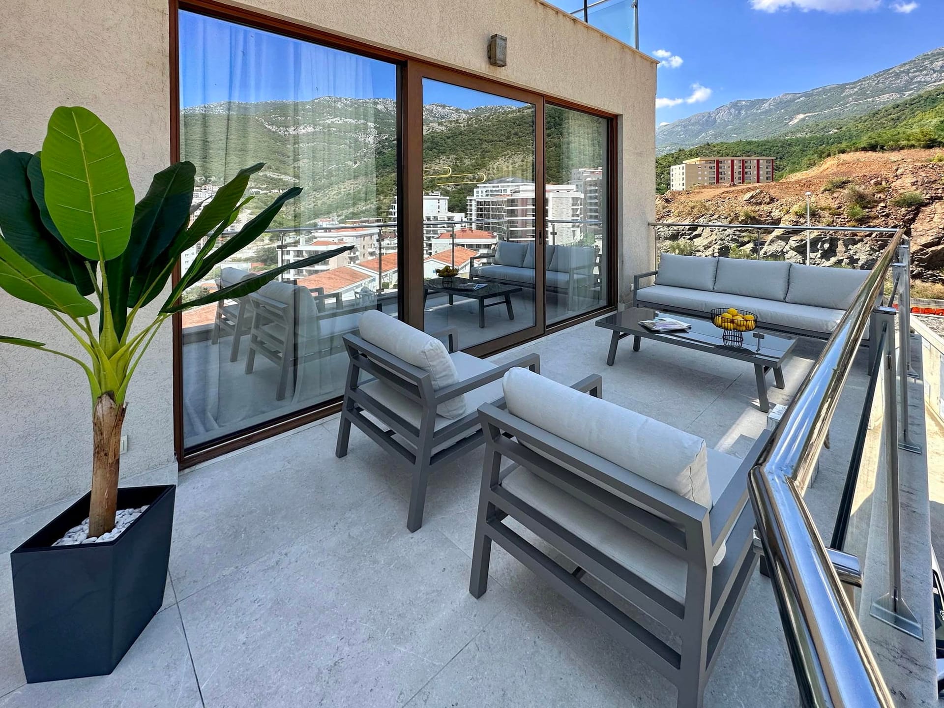 Spacious terrace with furniture and mountain views in a Becici apartment, Montenegro. Modern balcony with panoramic windows.