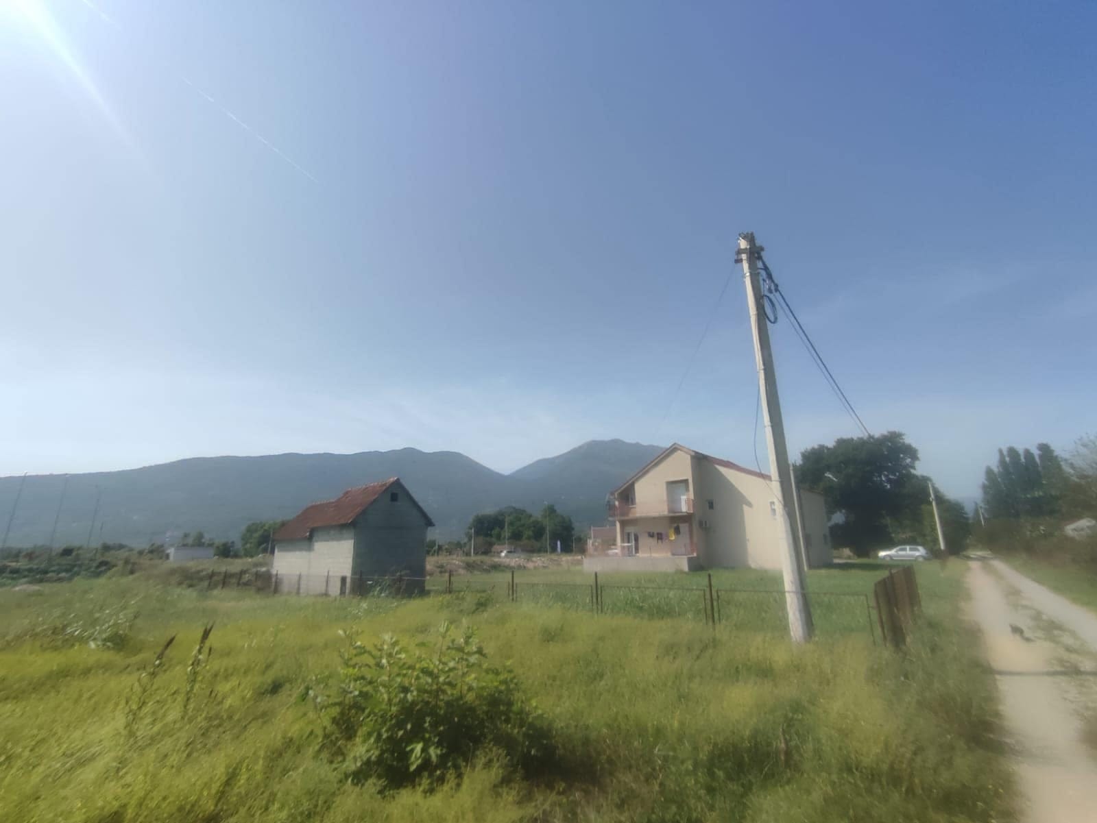 Two-story house with a plot and mountain views in Danilovgrad, Montenegro, against a backdrop of countryside and a road.