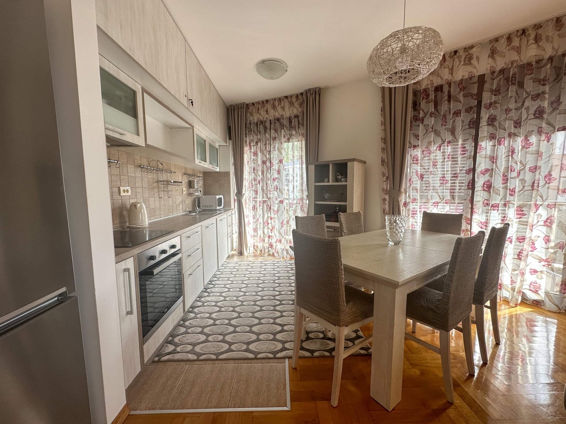 Modern kitchen and dining area in a Becici apartment, Montenegro: light-colored cabinetry, dining space, and balcony access.