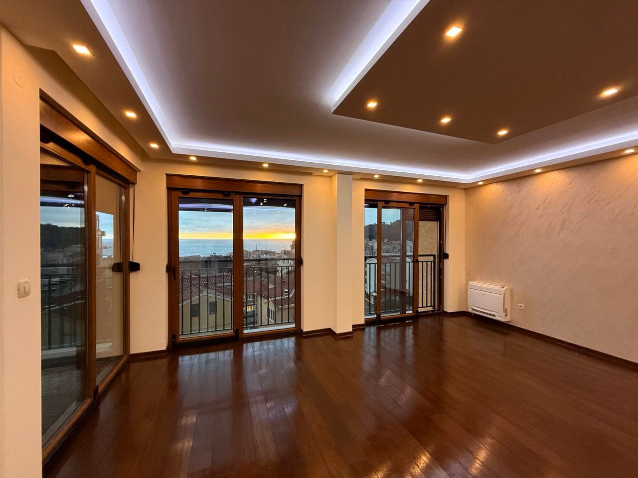 Living room in an apartment in Petrovac, Montenegro: parquet flooring, panoramic windows with sea views, and layered lighting.