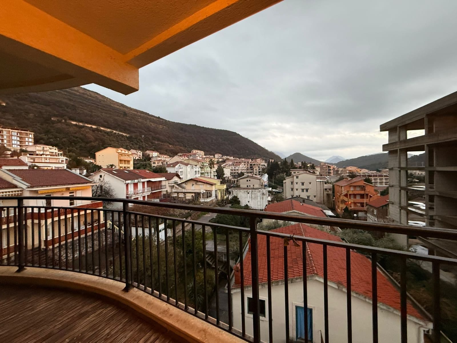 View from the apartment balcony in Petrovac, Montenegro: a city panorama, red rooftops, and a mountain landscape in the background.