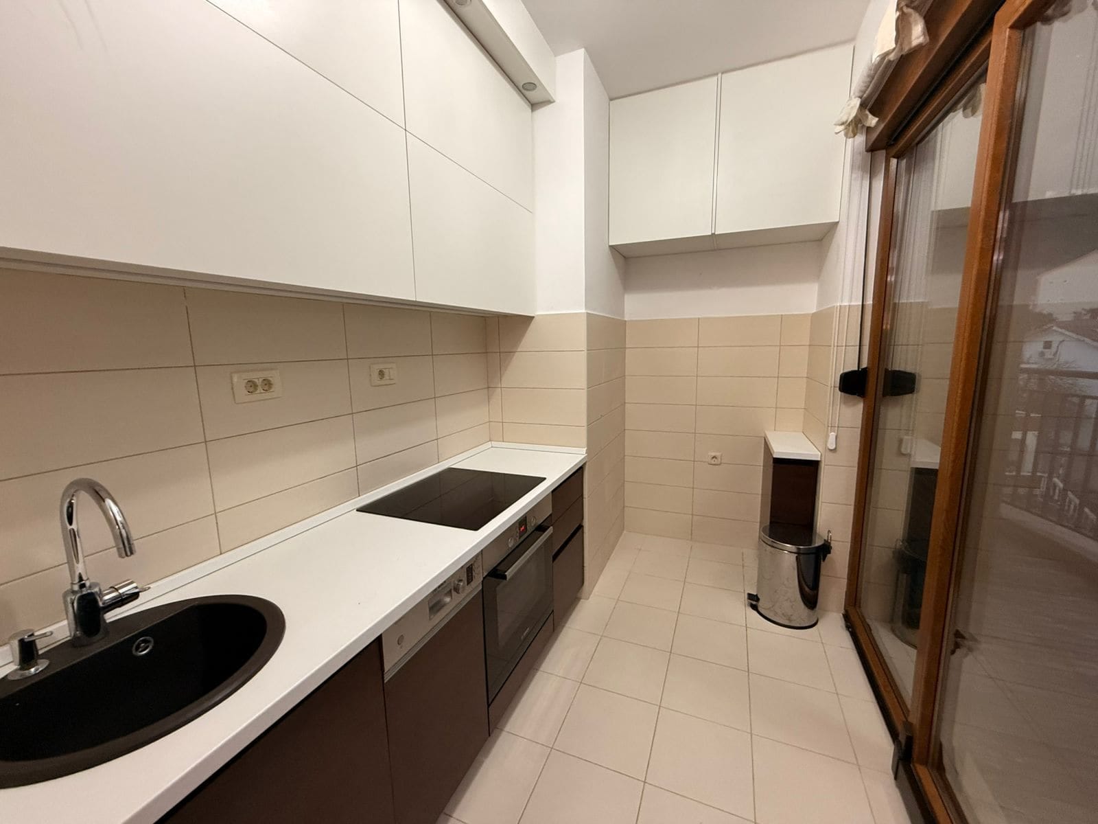 Modern kitchen in an apartment in Petrovac, Montenegro: white cabinetry, built-in appliances, and access to the balcony.