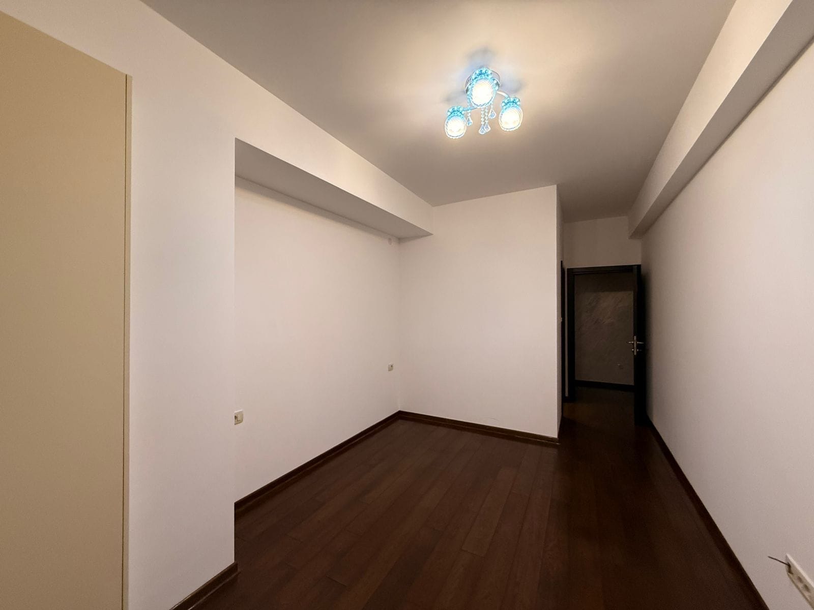 Bright living room with dark parquet in an apartment for sale in Petrovac, Montenegro. Empty room with white walls.