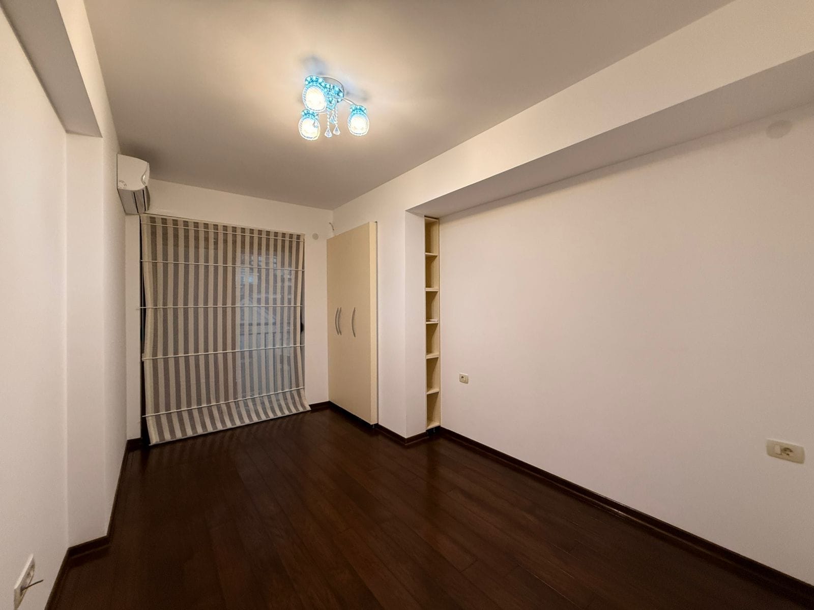 Bright bedroom with dark parquet flooring, built-in wardrobe, and air conditioner in an apartment, Petrovac, Montenegro.