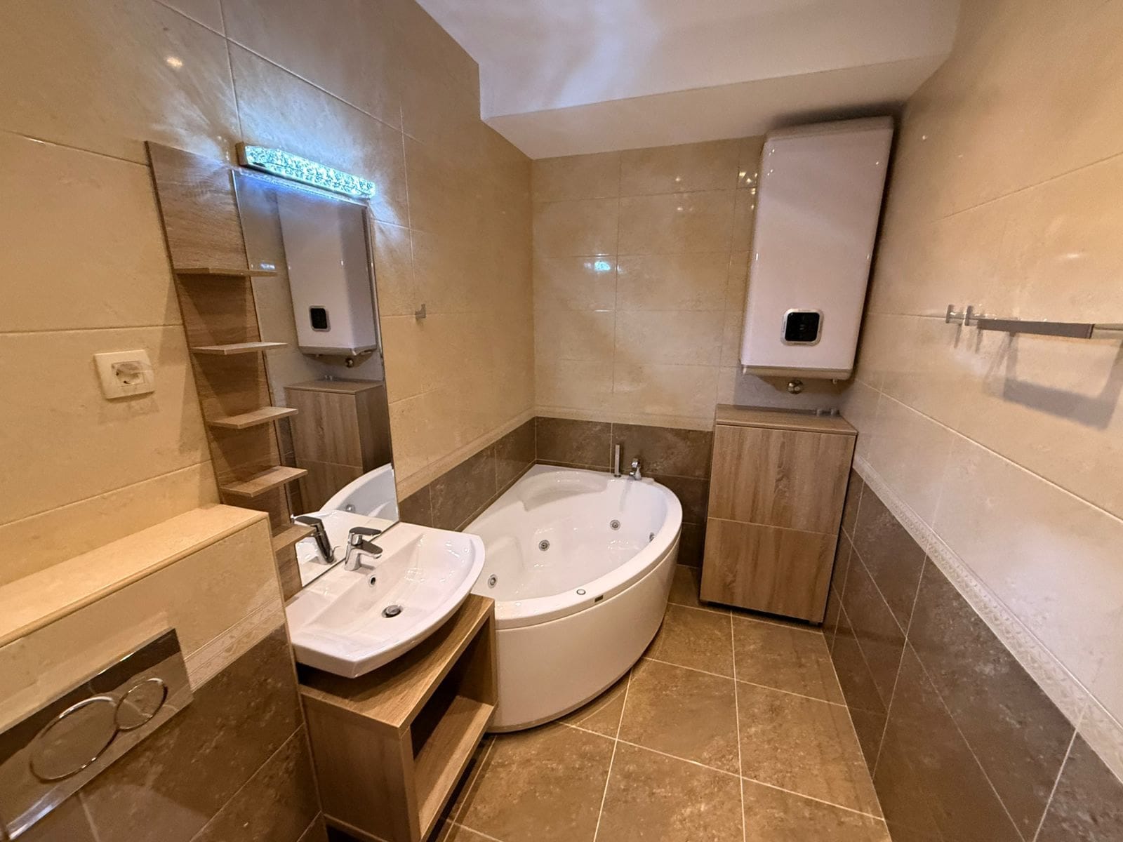 Bathroom in an apartment in Petrovac, Montenegro: corner jacuzzi, beige tiles, vanity with sink, and boiler.