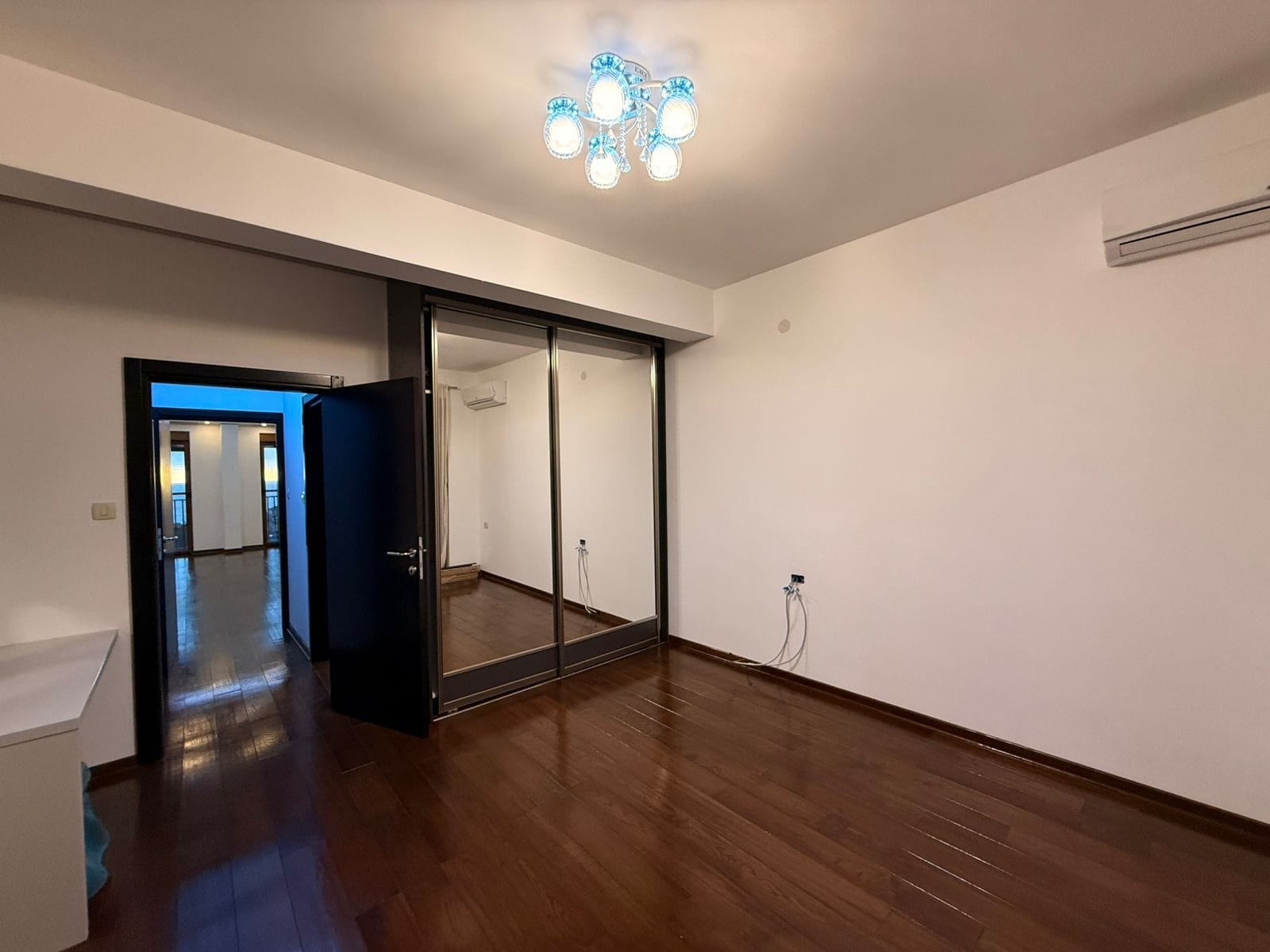 Bedroom in an apartment in Petrovac, Montenegro: mirrored sliding wardrobe, dark parquet flooring, air conditioner, and a stylish chandelier.