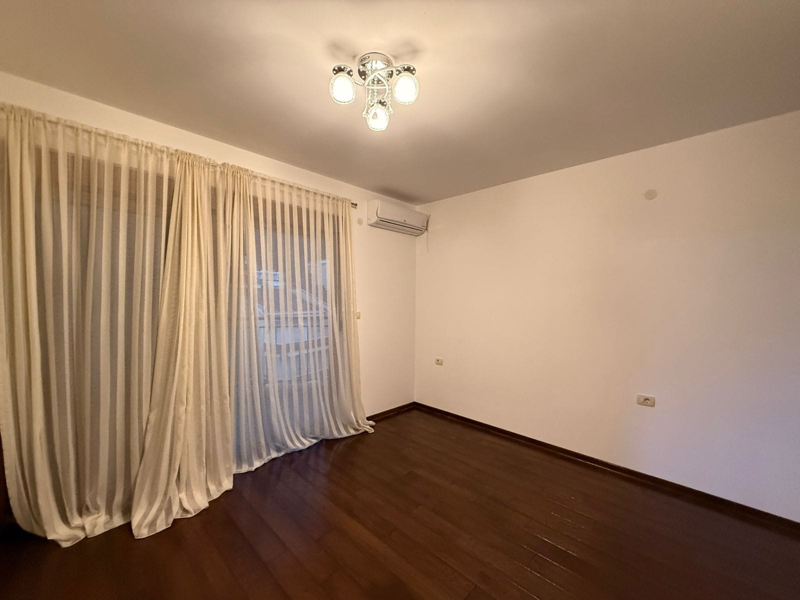 Bright living room with dark parquet flooring, air conditioning, and floor-to-ceiling curtains in an apartment, Petrovac, Montenegro.