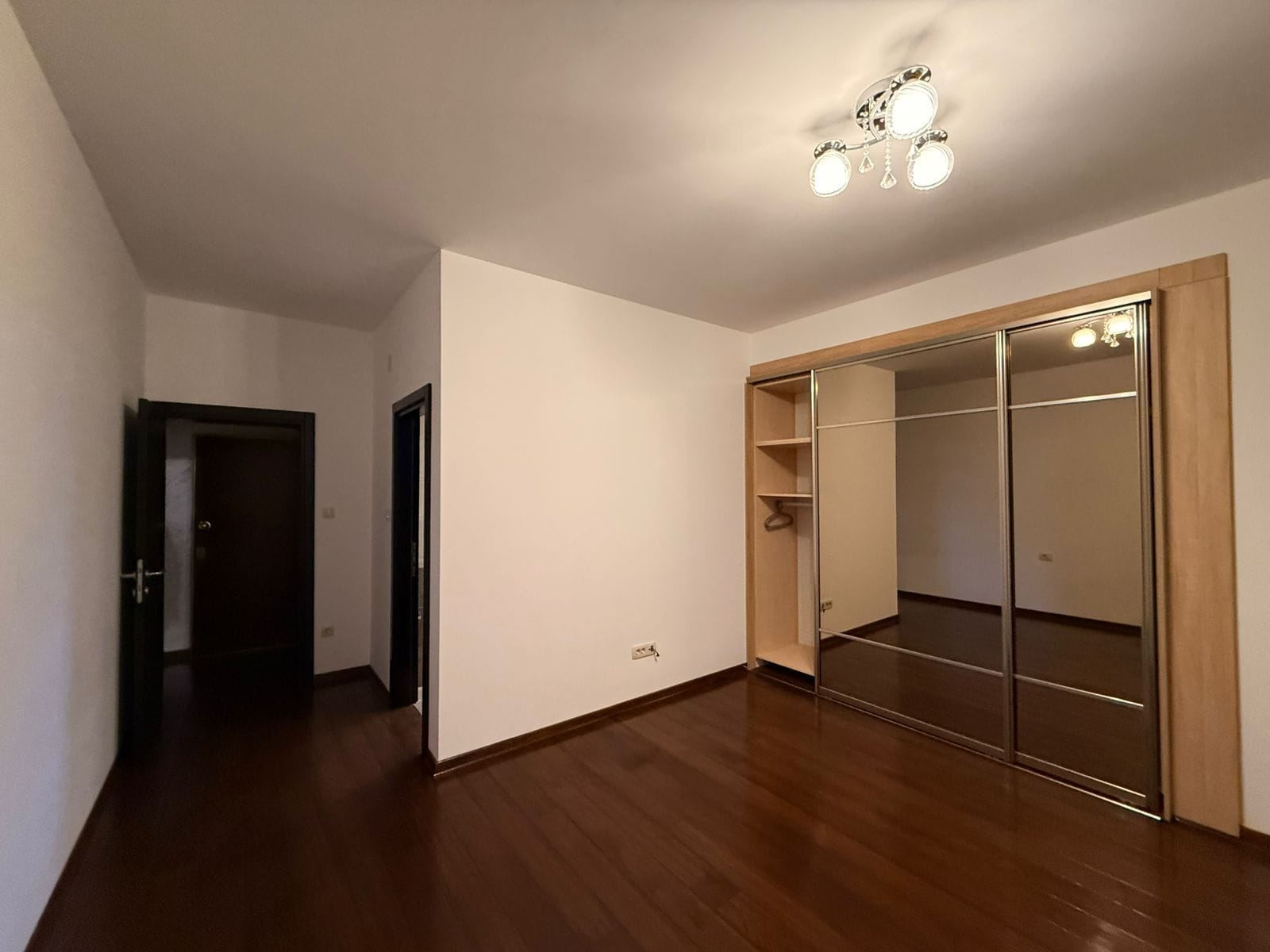 Bedroom in an apartment in Petrovac, Montenegro: a bright room with dark parquet flooring and a built-in mirrored sliding wardrobe.