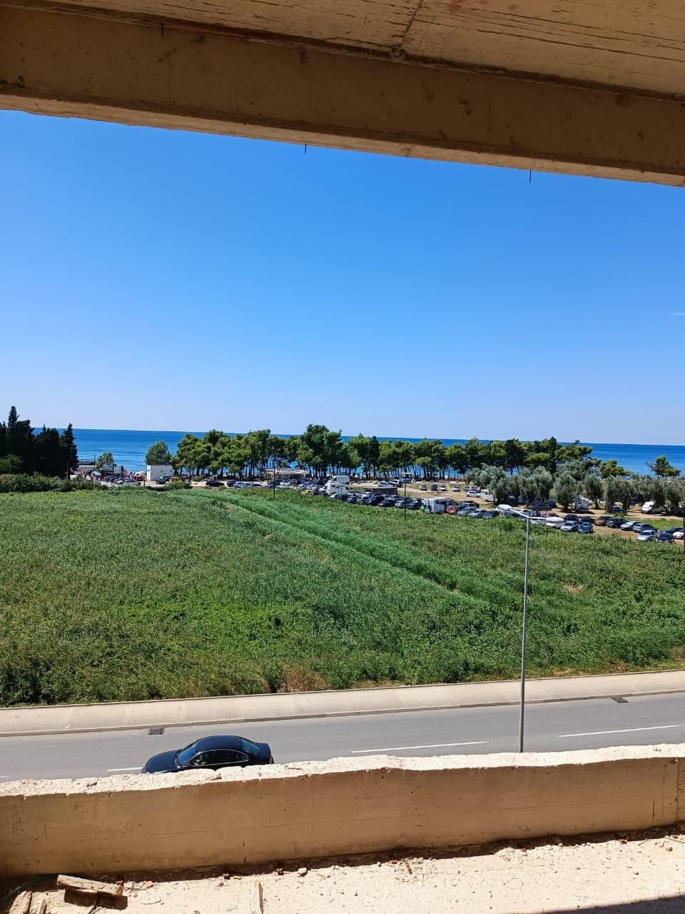 View from the balcony of a residential complex in Shushan, Montenegro: a panorama of the sea, green area, and road.