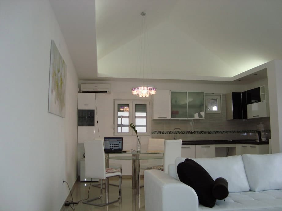 Modern living room with kitchen in a house in Krašići, Montenegro: white sofa, dining area, and stylish lighting.
