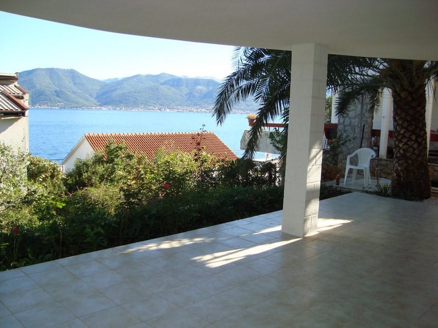 Terrace with sea and mountain views in a house in Krašići, Montenegro: tiled floor, palm tree, and panoramic scenery.