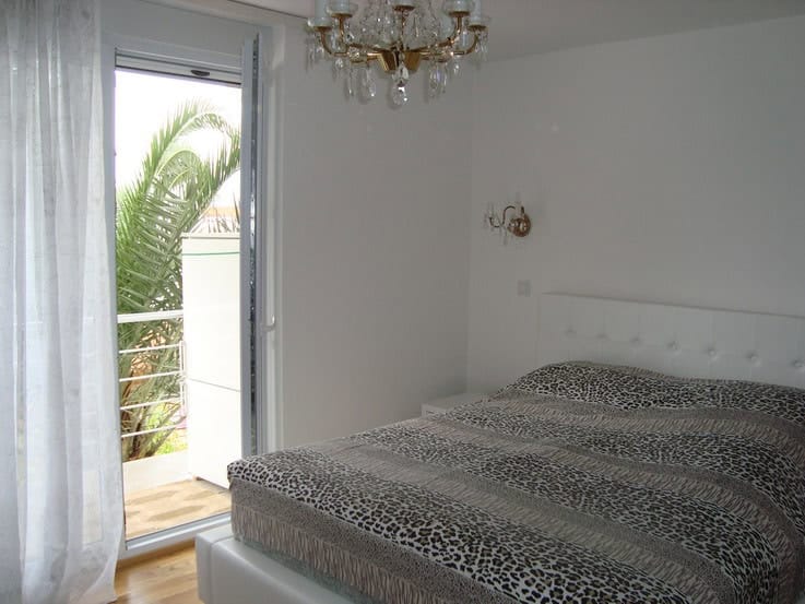 Bedroom with a double bed and access to a balcony overlooking palm trees in a house, Krašići, Montenegro.