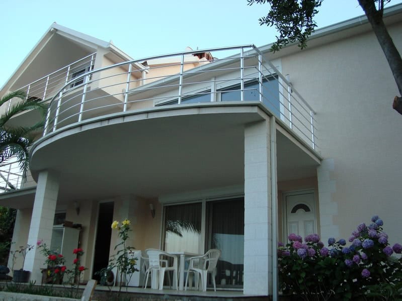 House facade in Krašići, Montenegro: terrace with garden furniture, panoramic windows, and a balcony with a metal railing.