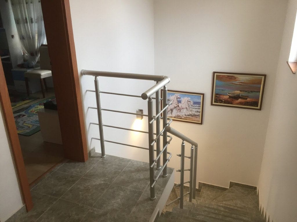 Staircase with metal railings in a two-story apartment in Bar, Montenegro, with paintings on the walls.