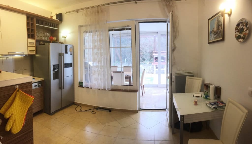 Kitchen with dining area in an apartment in Bar, Montenegro: light-colored furniture, access to the terrace, and garden view.