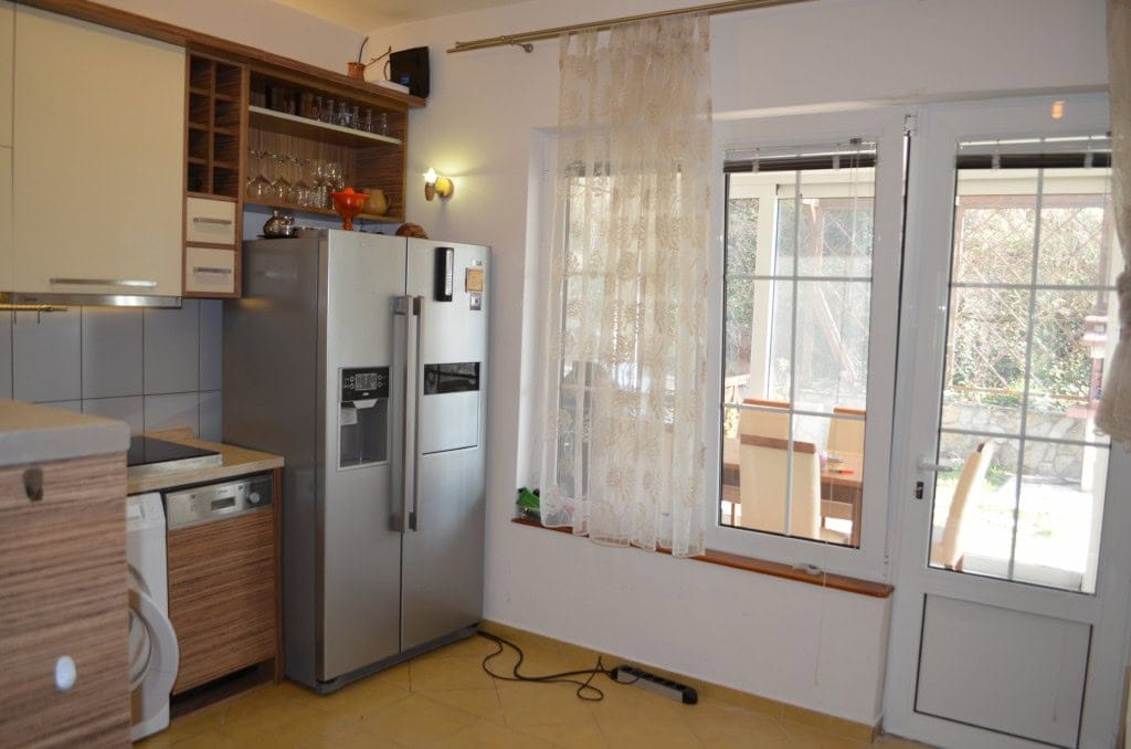 Kitchen in an apartment in Bar, Montenegro: light-colored furniture, a large refrigerator, and access to the terrace.