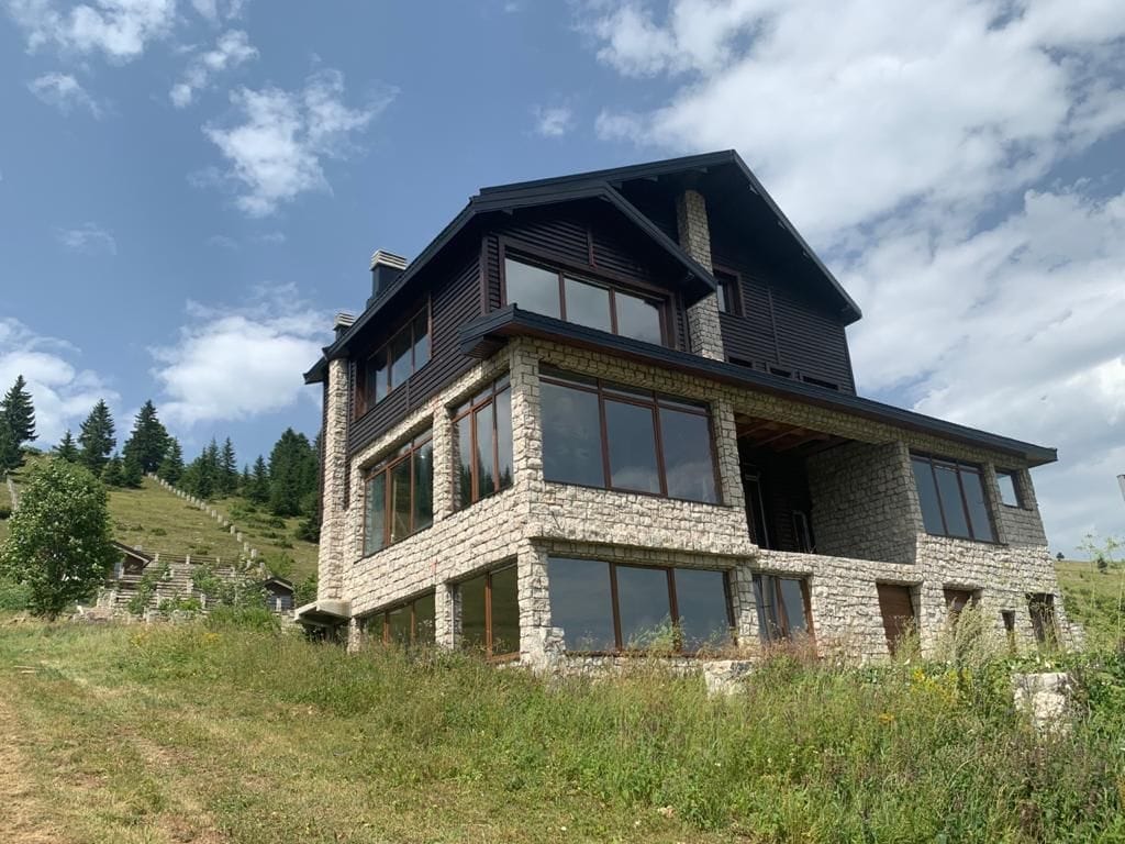 Three-story villa in the mountains of Žabljak, Montenegro: natural stone and dark wood facade, panoramic windows.