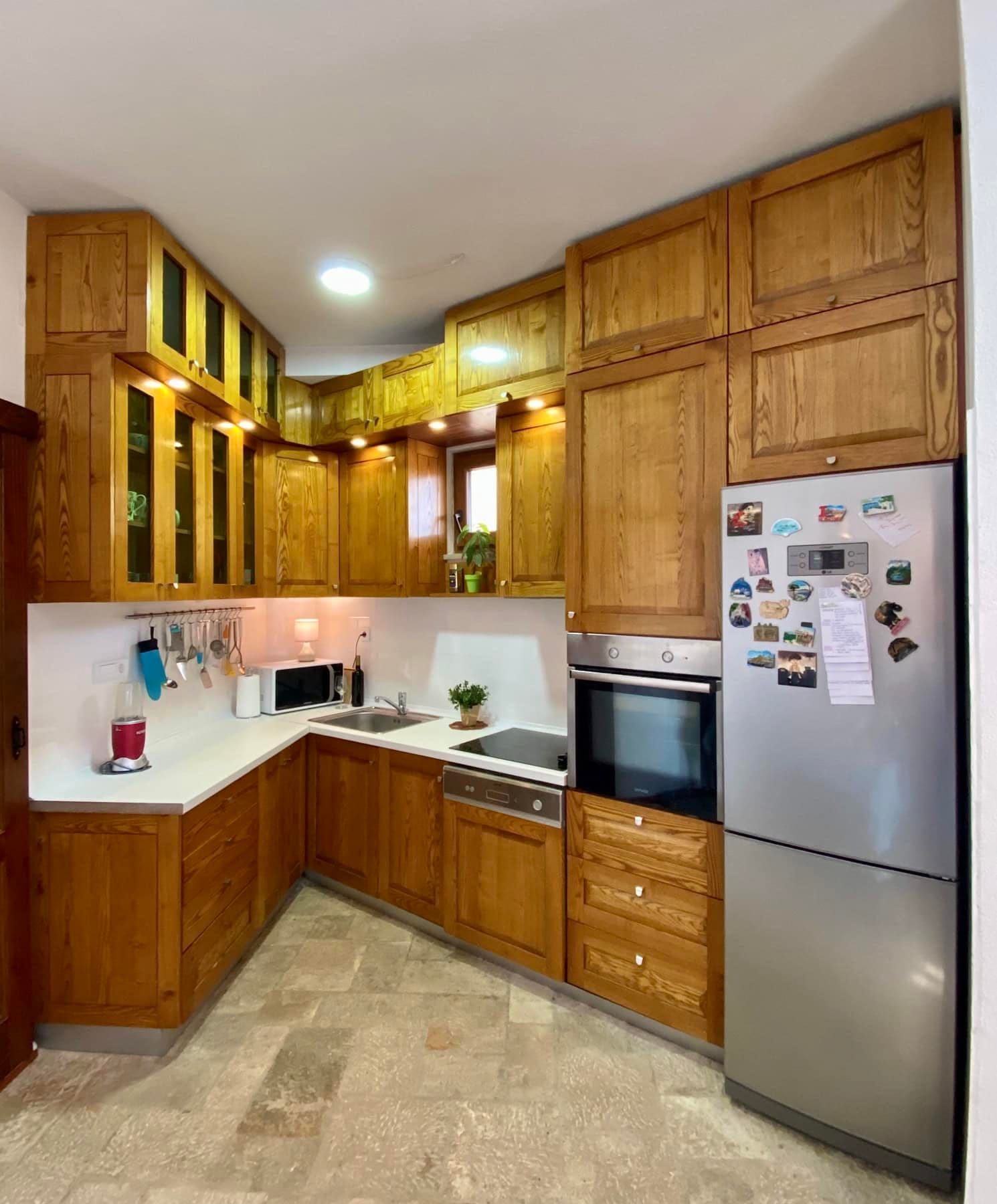 Corner kitchen made of solid wood with modern appliances in a house, Shushan, Montenegro. Light countertop and stone floor.