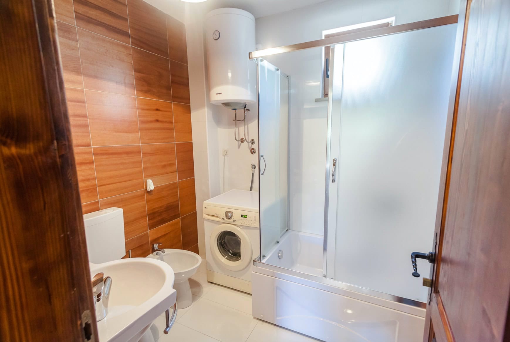 Bathroom in a house in Shushan, Montenegro: shower cabin, washing machine, water heater, and wood-look tile finish.