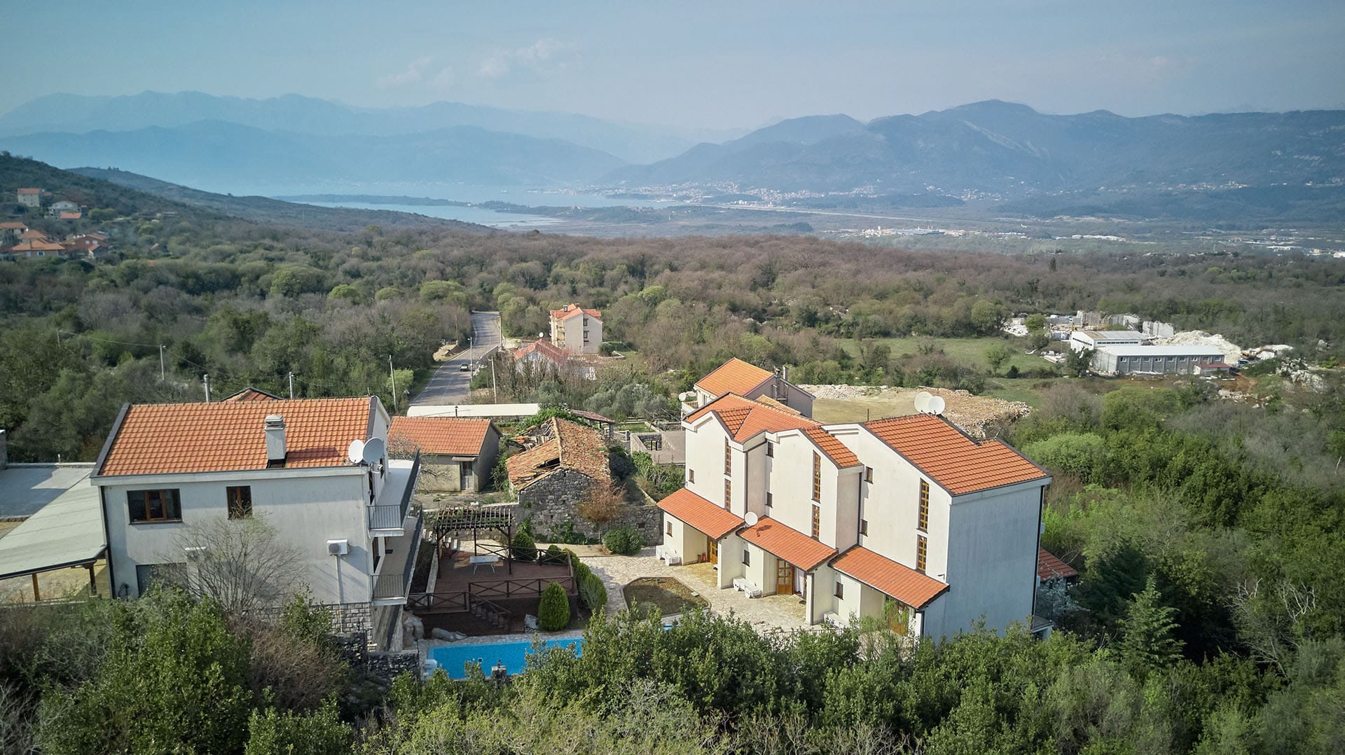 Aerial view of townhouses with a pool in Vranovici village, Bigovo, Montenegro, with mountains and a sea bay in the background.