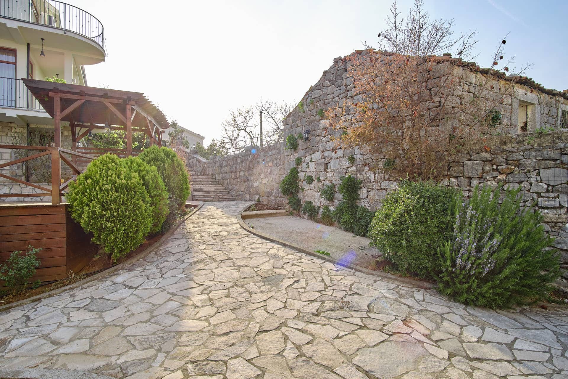 Townhouse courtyard in Bigovo, Montenegro: stone path, old stone wall, gazebo, and landscaping.