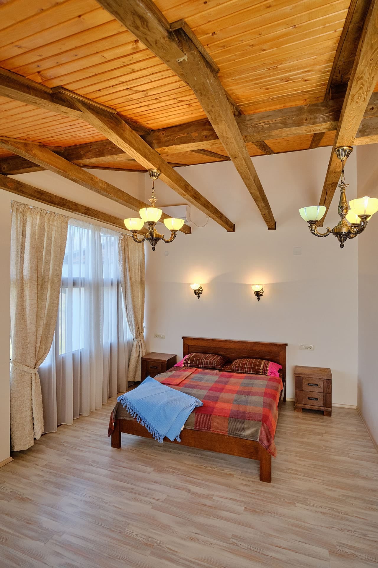 Bedroom in a townhouse in Bigovo, Montenegro: wooden ceiling beams, a double bed, and classic chandeliers.